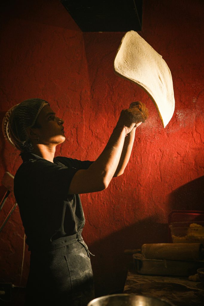 A chef skillfully tosses pizza dough in a warmly lit kitchen, showcasing traditional culinary artistry.